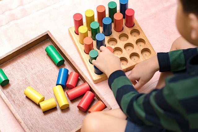 Closeup: Hands of a little Montessori kid (3-6) learning about size, orders, sorting, arranging by engaged colorful wooden sensorial blocks. Educational toys, Cognitive skills, Montessori activity.