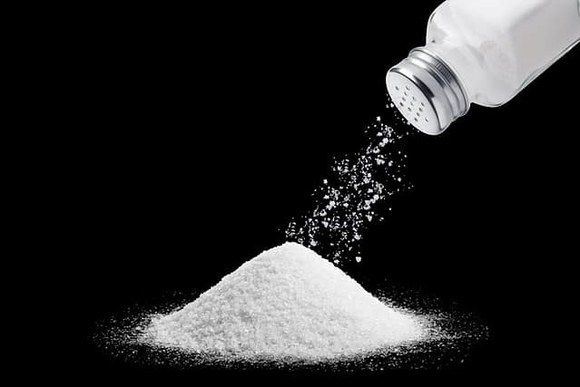 image of salt powder piled on a black background in the upper right corner a bottle of salt sprinkled with salt powder out of the bottle onto the pile of salt below. Suitable for use in food media.