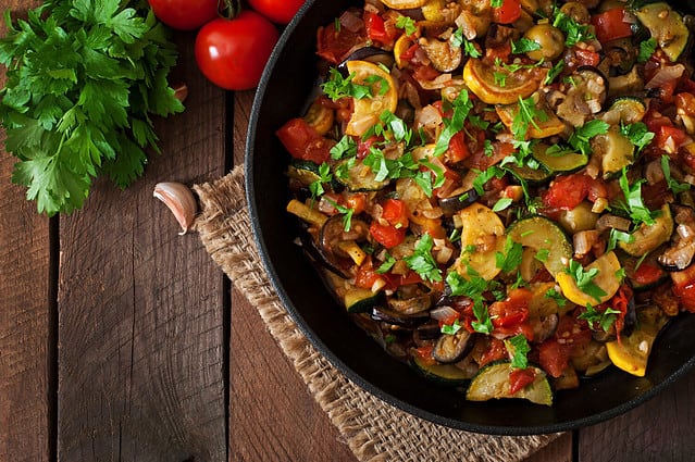 Vegetable Ratatouille in frying pan on a wooden table. Top view